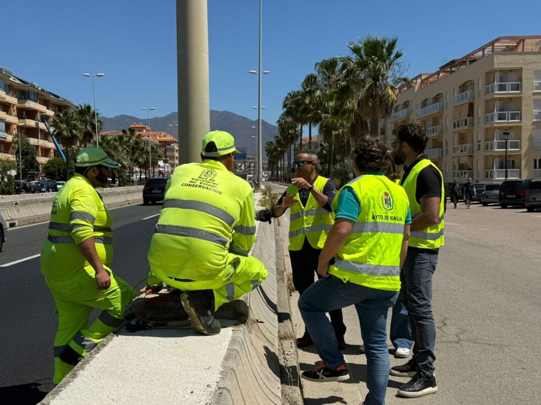 Trabajadores y técnicos con chalecos reflectantes conversan junto a una carretera urbana